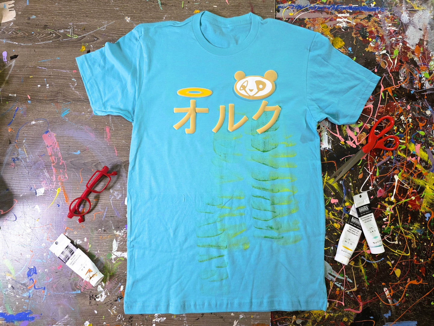 Blue t-shirt with yellow text and green design on a messy table.