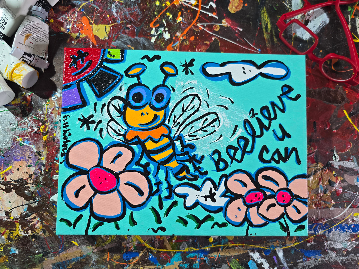 Colorful painting of a bee and flowers on a textured surface with art supplies.